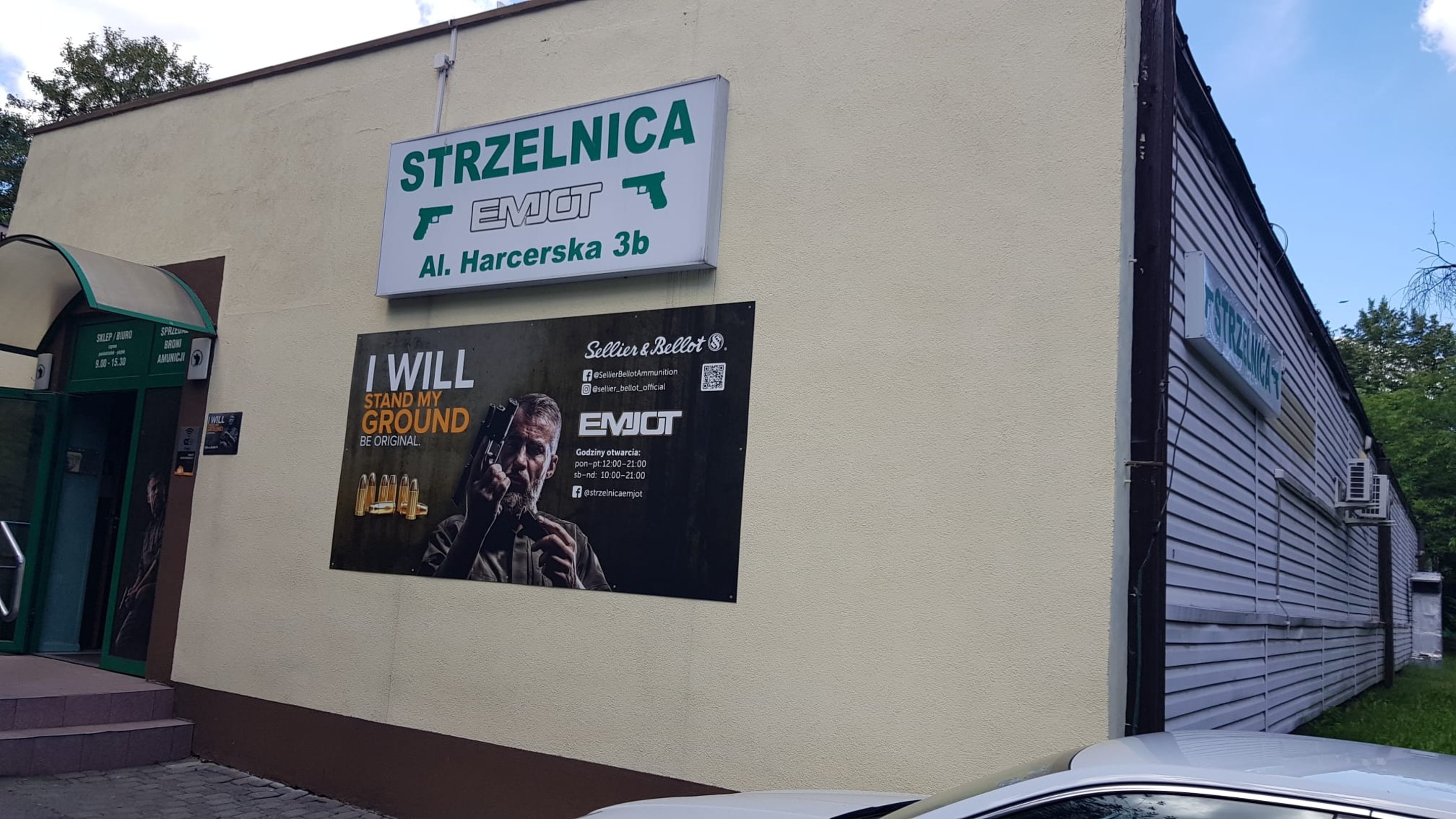 Wejście do Strzelnicy EMJOT przy Al. Harcerskiej 3b. Budynek strzelnicy z szyldem i reklamą Sellier & Bellot