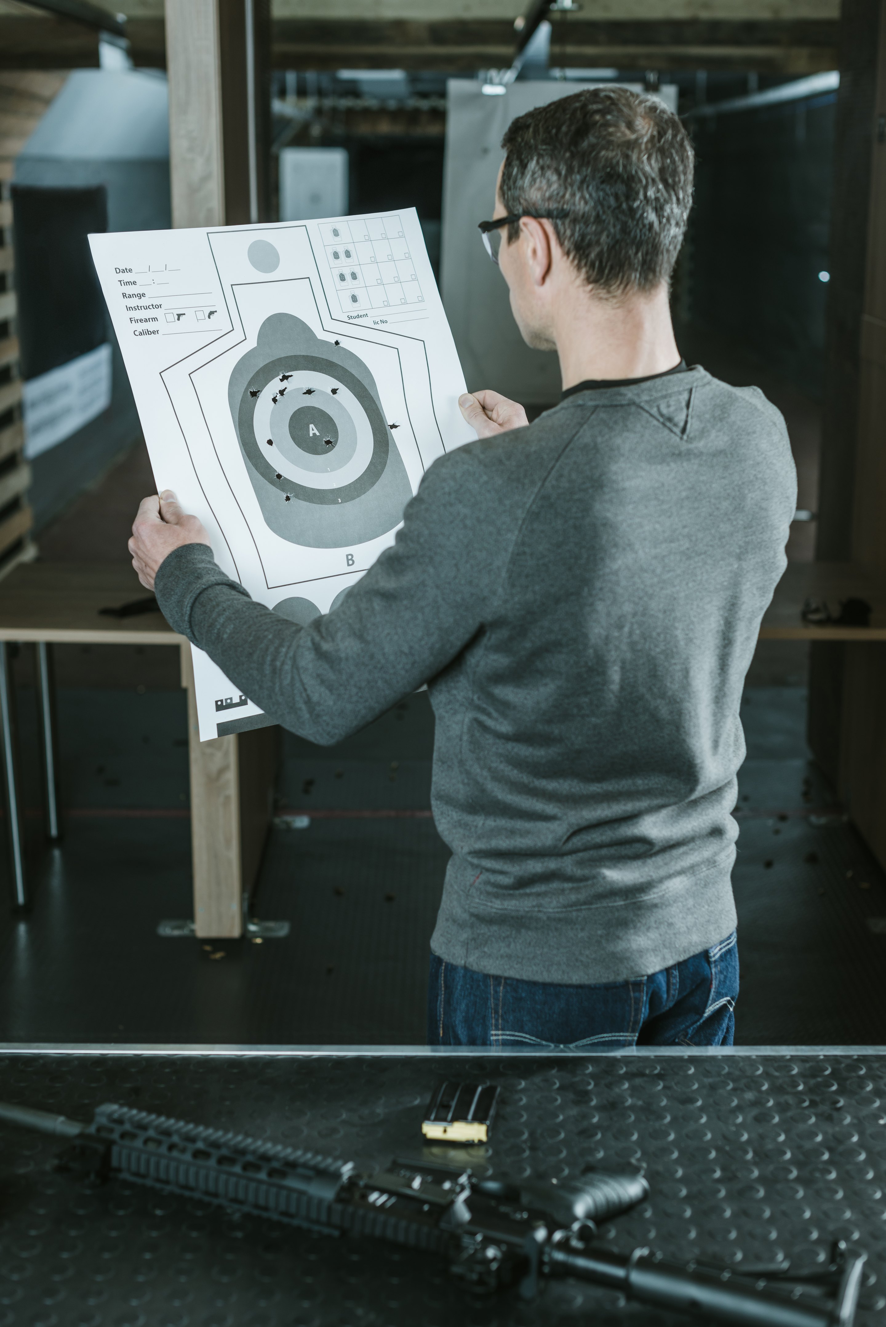 Karabin i magazynek na stole podczas kursu Broń Długa Level 1 w Strzelnicy EMJOT. Uczestnik analizuje wyniki strzelania.